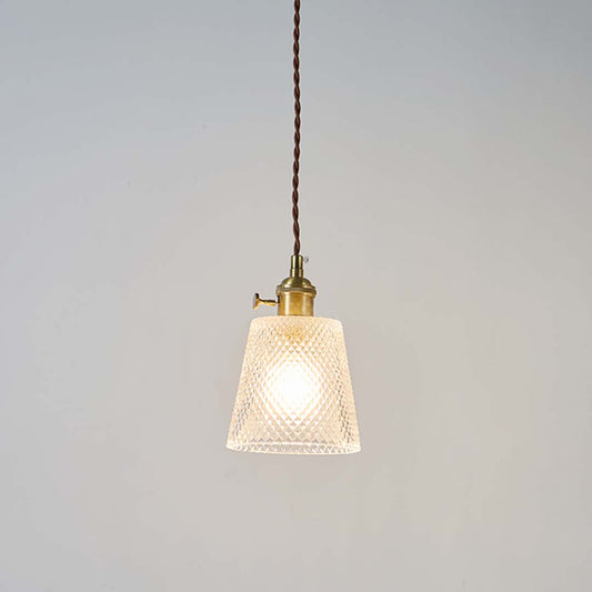 Textured clear glass pendant light with brass top and brown cord glowing warmly on white background for home interiors.