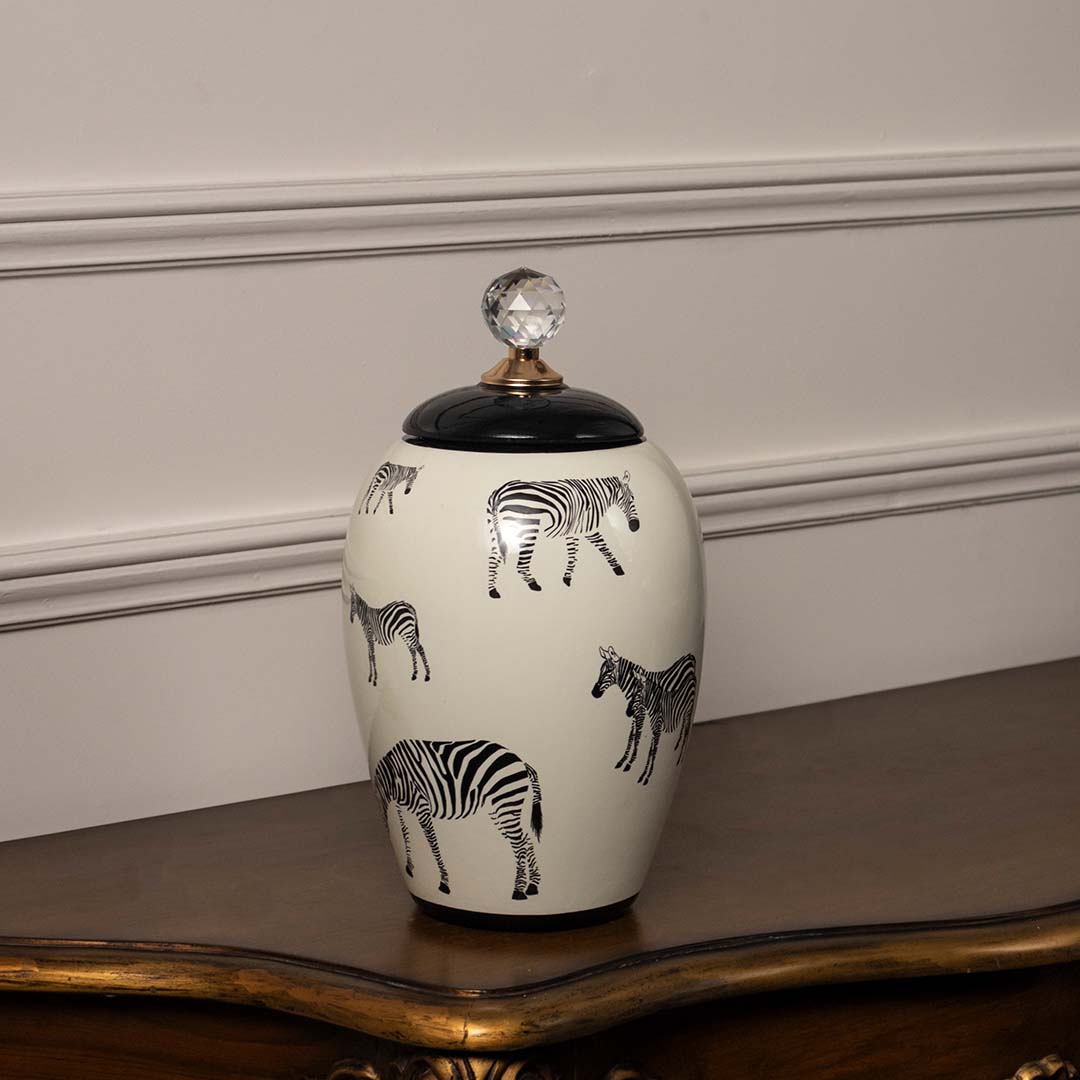 White ceramic jar with black animal artwork and crystal knob lid placed on wooden table against neutral wall background showcasing artistic modern home decor styling.