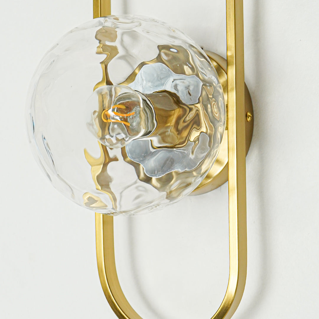 Closeup of gold metal wall light with sculpted glass shade showcasing artistic texture and premium finish for modern interior decor styling.