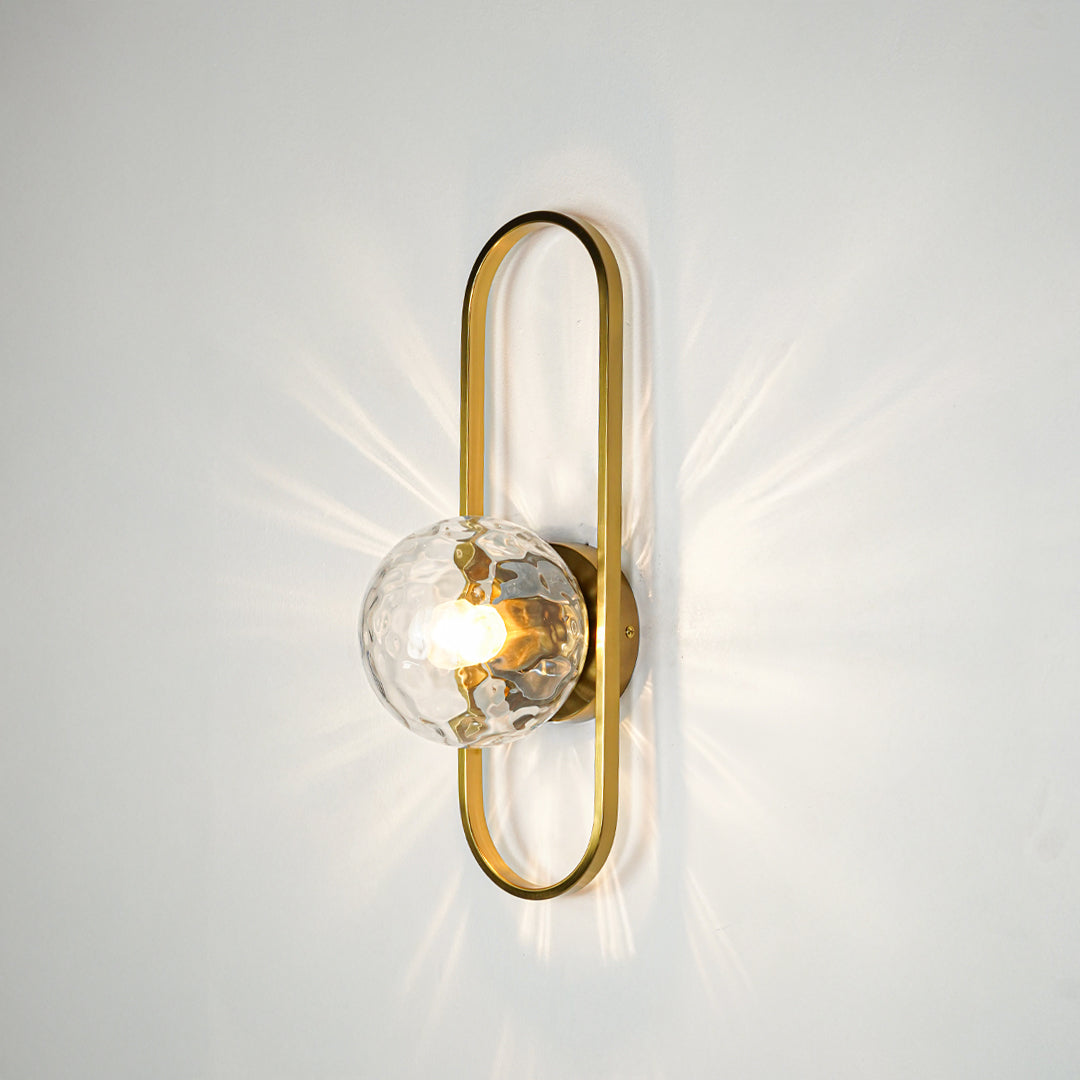 Gold finish wall light with clear sculpted glass shade emitting warm glow ideal for elegant bedroom or hallway wall decor placement.