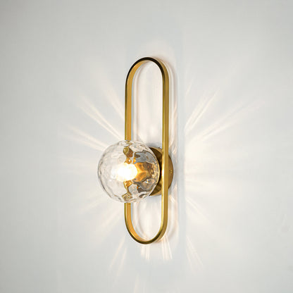 Gold finish wall light with clear sculpted glass shade emitting warm glow ideal for elegant bedroom or hallway wall decor placement.