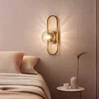 Modern wall light with glass bulb and gold frame casting warm glow styled beside bed creating cozy ambient lighting for home decor.