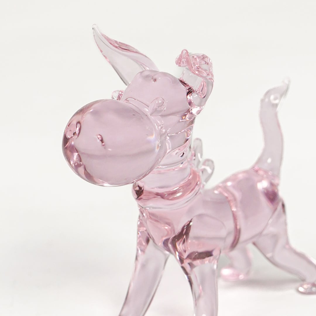 Detailed closeup of pink glass dog figurine showcasing glossy surface and playful sculpted form.