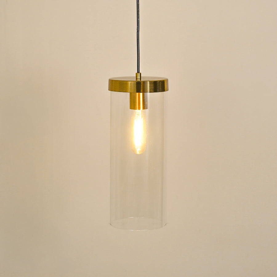 Clear glass tube pendant light with brushed brass accents illuminated for elegant ceiling decor.