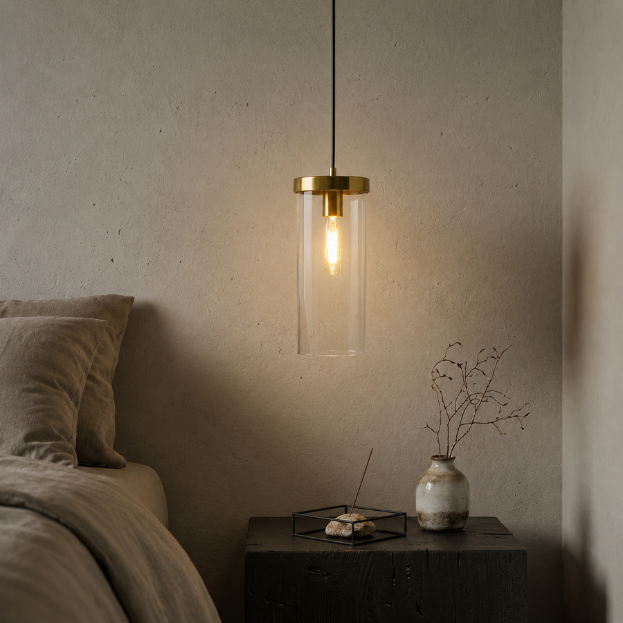 Brass and glass wall light casting warm glow beside bed in sophisticated bedroom interiors.