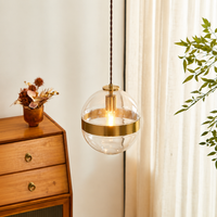 Lifestyle image of glass globe gold metal hanging pendant light for modern living room decor styling with bright finish.