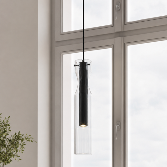 A modern black pendant light with a ribbed clear glass bottle-shaped shade hanging in front of a large window.