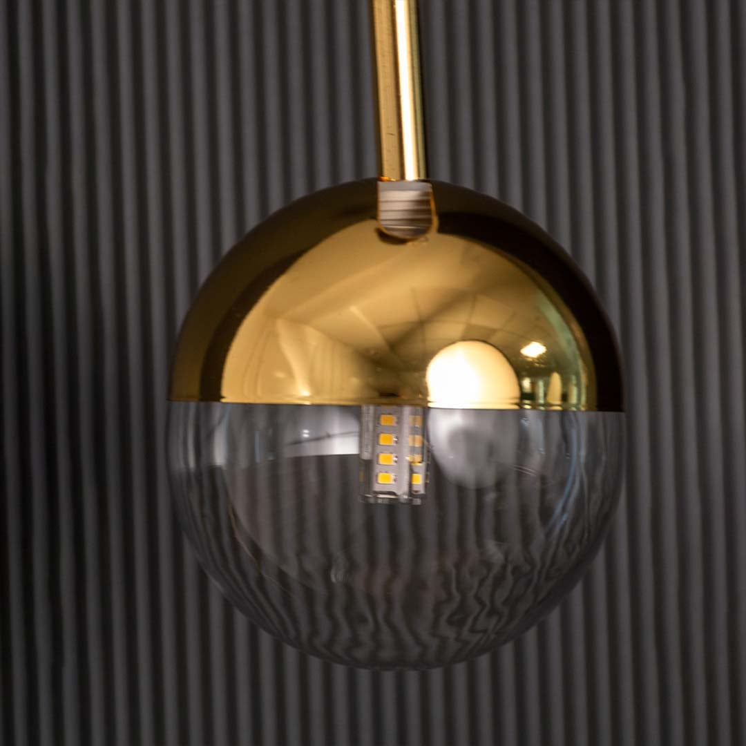 A closeup view of the modern pendant light showing the gold dome top and clear glass lower half with detailed reflections capturing its smooth polished finish.