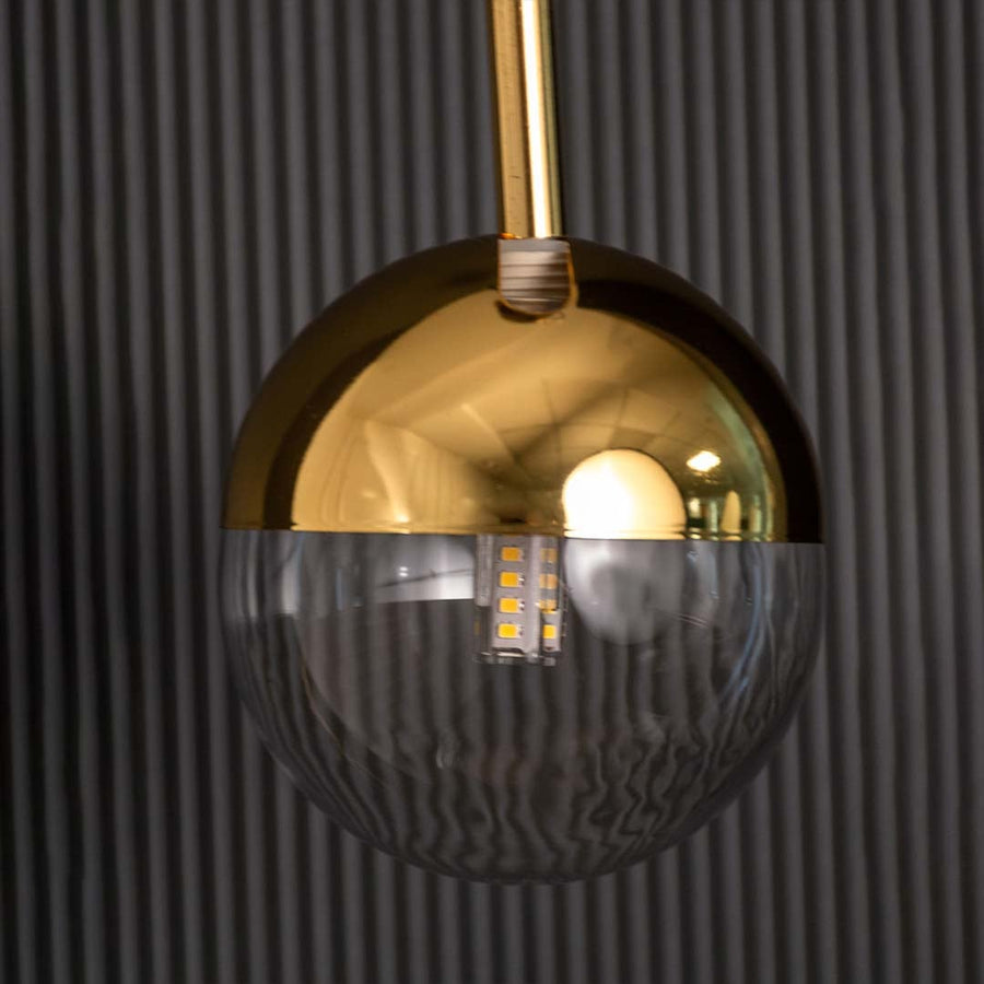 A closeup view of the modern pendant light showing the gold dome top and clear glass lower half with detailed reflections capturing its smooth polished finish.