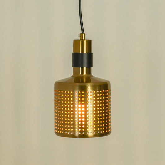 A modern pendant light with a cylindrical brass shade covered in a grid of small circular cutouts, casting a warm glow from within. It features a black band near the top and hangs from a black cord against a neutral, light beige background.