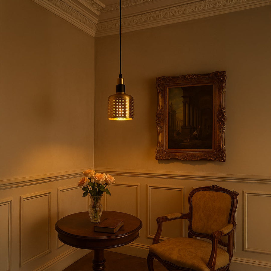 A gold perforated pendant light with lights on illuminating a contemporary blue accent wall setting perfect for dining areas lounges and modern interiors.