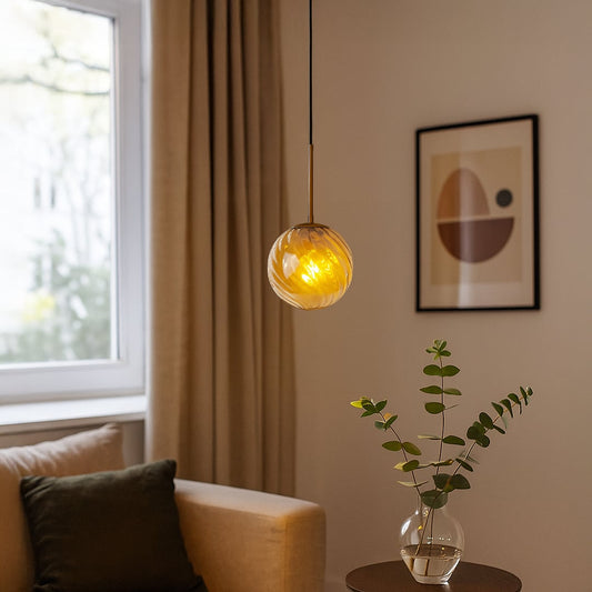 A modern gold and amber glass pendant light glowing warmly in a cozy living room creating soft ambient lighting ideal for sofas corners and reading spaces.