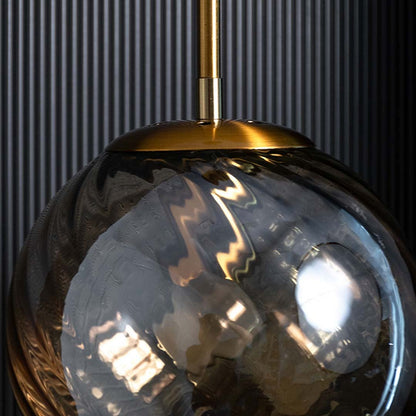 A closeup of the gold and amber pendant light showing the swirled textured glass and warm reflective glow ideal for modern elegant interiors.