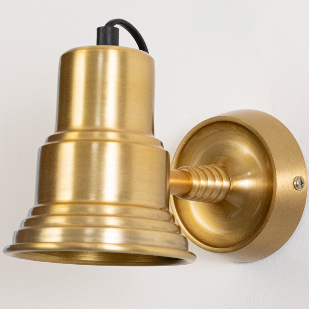 Closeup of classic gold metal wall light highlighting bell shaped shade circular backplate and smooth polished finish.