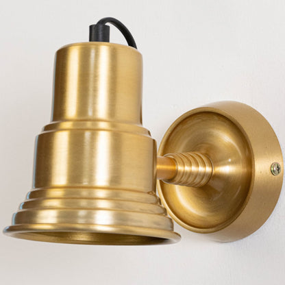 Closeup of classic gold metal wall light highlighting bell shaped shade circular backplate and smooth polished finish.
