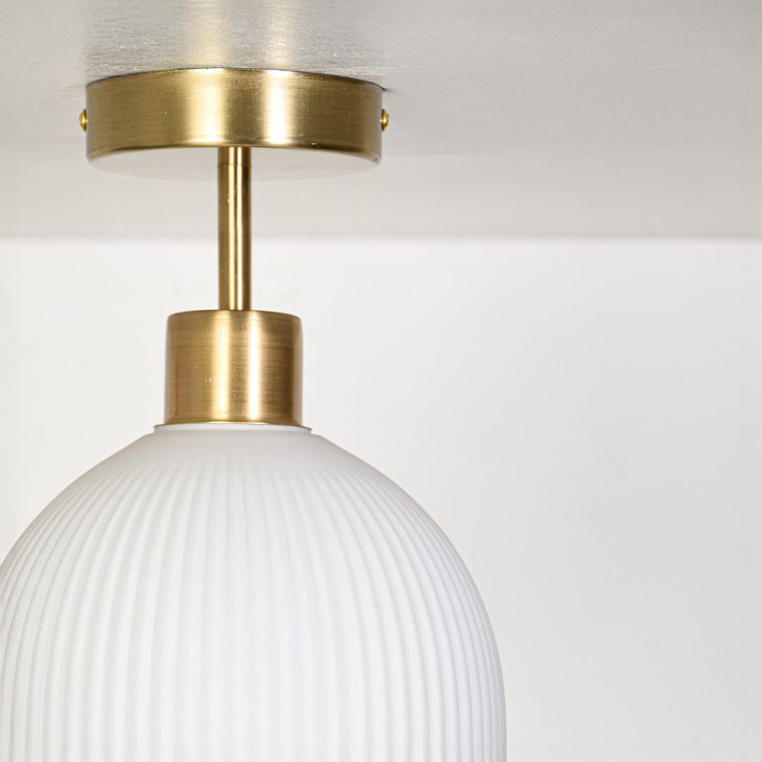 Closeup of gold metal ceiling light mount with ribbed white glass shade showing refined craftsmanship and smooth detailing.