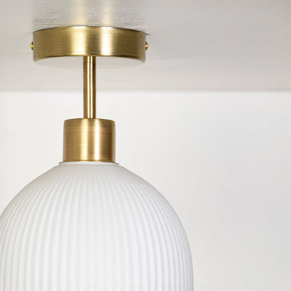 Closeup of gold metal ceiling light mount with ribbed white glass shade showing refined craftsmanship and smooth detailing.