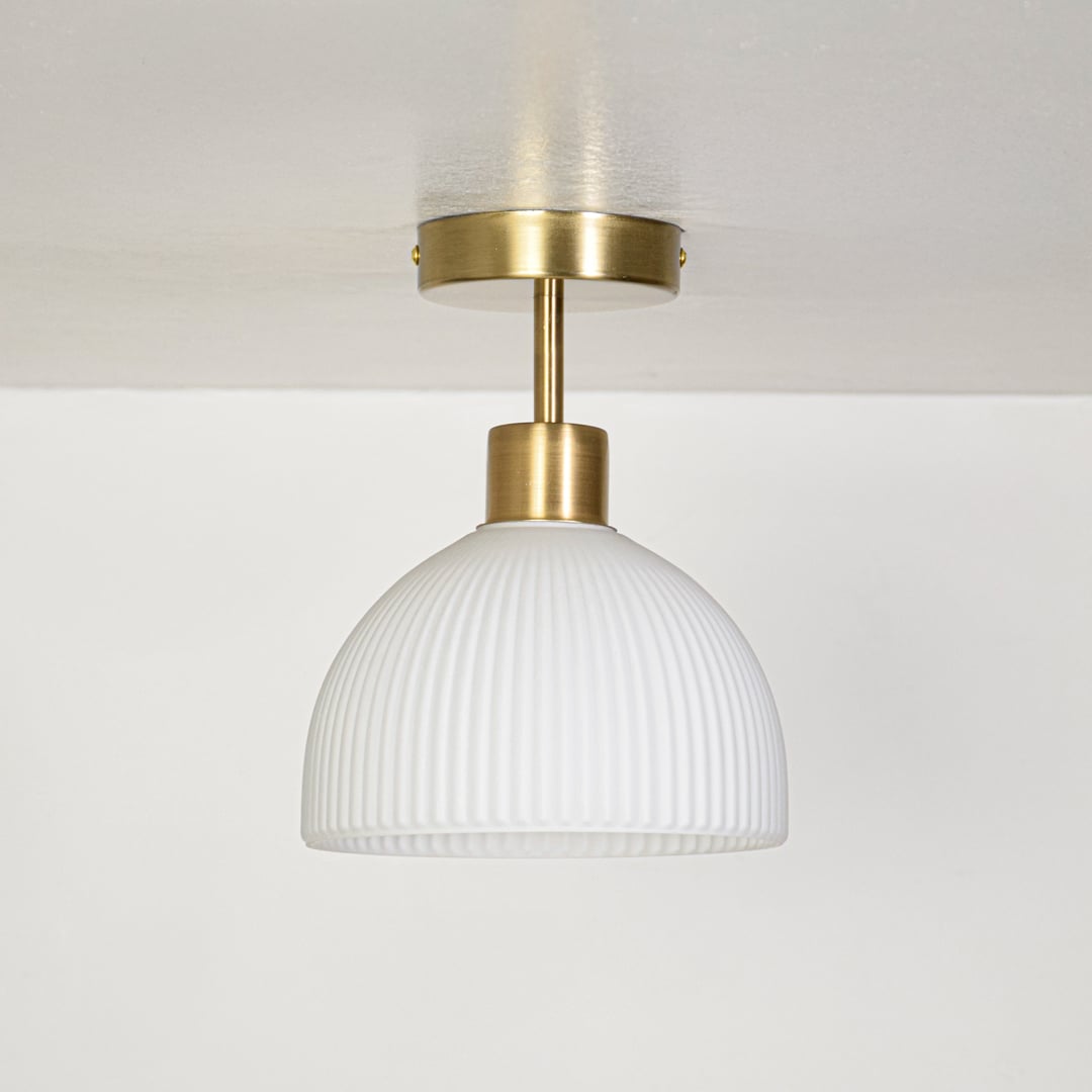 Minimal ceiling pendant light with ribbed white glass shade and gold metal canopy displayed on off white background.