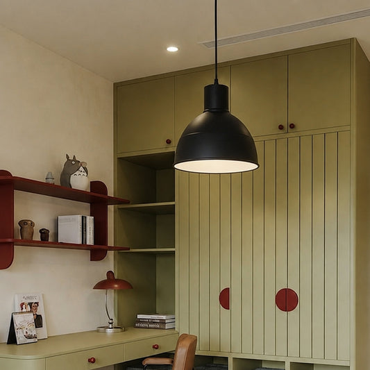A modern black dome pendant light hanging in a styled home office with sage green cabinets, a wooden desk, and red accents.
