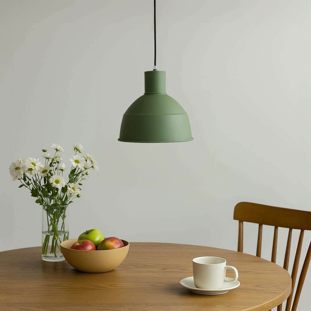 Matte green metal dome pendant light hanging over a round wooden dining table with fresh white flowers for a modern breakfast nook decor.