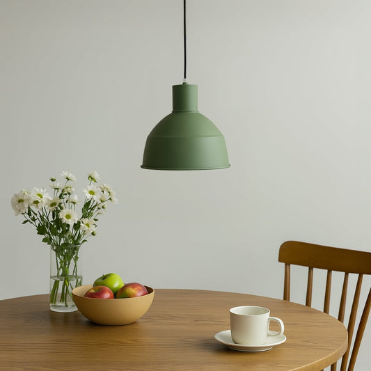 Matte green metal dome pendant light hanging over a round wooden dining table with fresh white flowers for a modern breakfast nook decor.