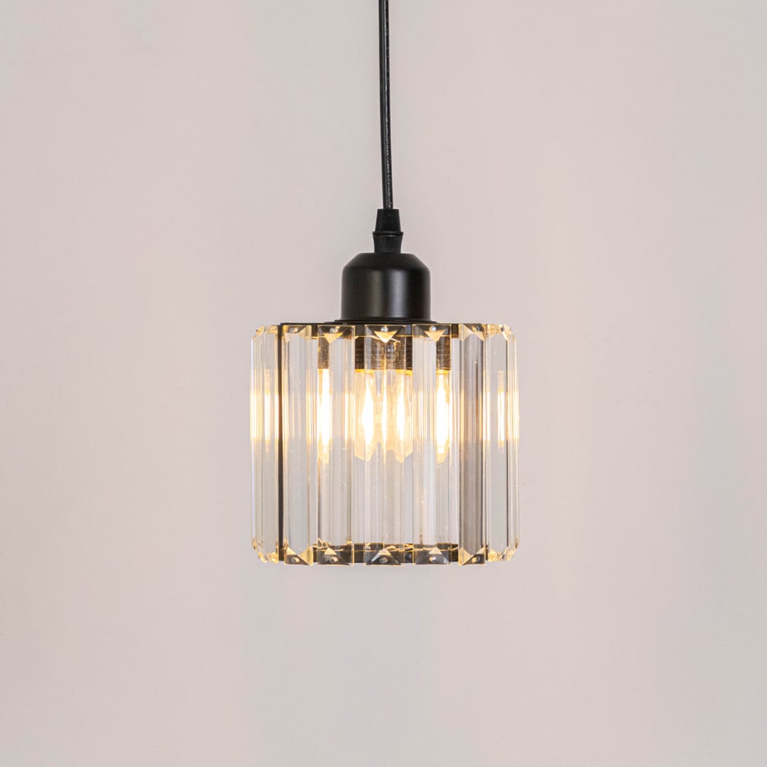 Glass pendant light with black metal fixture glowing warmly against plain white background.