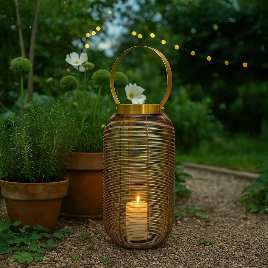 Gold metal wire mesh lantern with circular handle illuminated with candle on outdoor garden patio stone path at dusk.