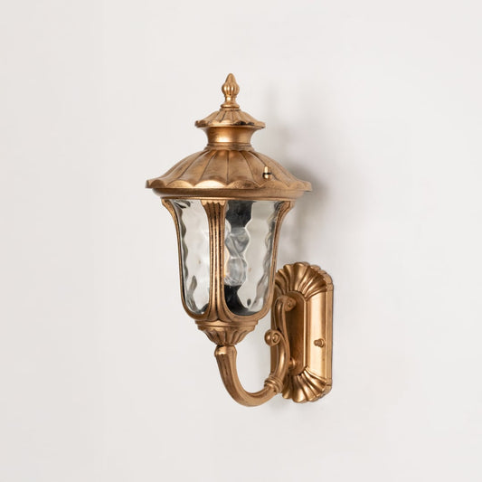 Gold finish exterior wall lantern turned off on white background showing detailed metal body curved arm and textured glass panels clearly.