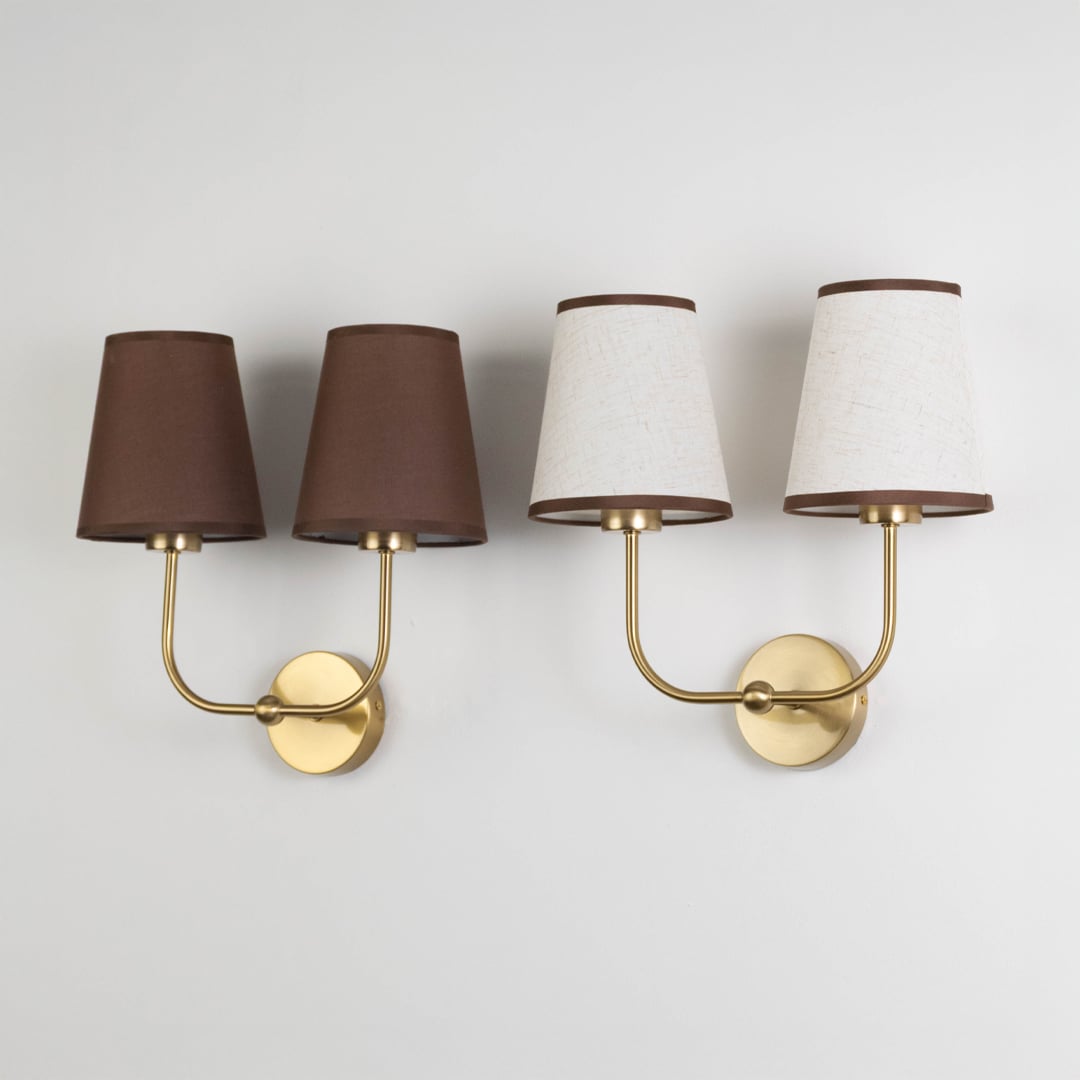 Double wall sconce with gold metal frame and cream textured shades shown on a white background with lights off.