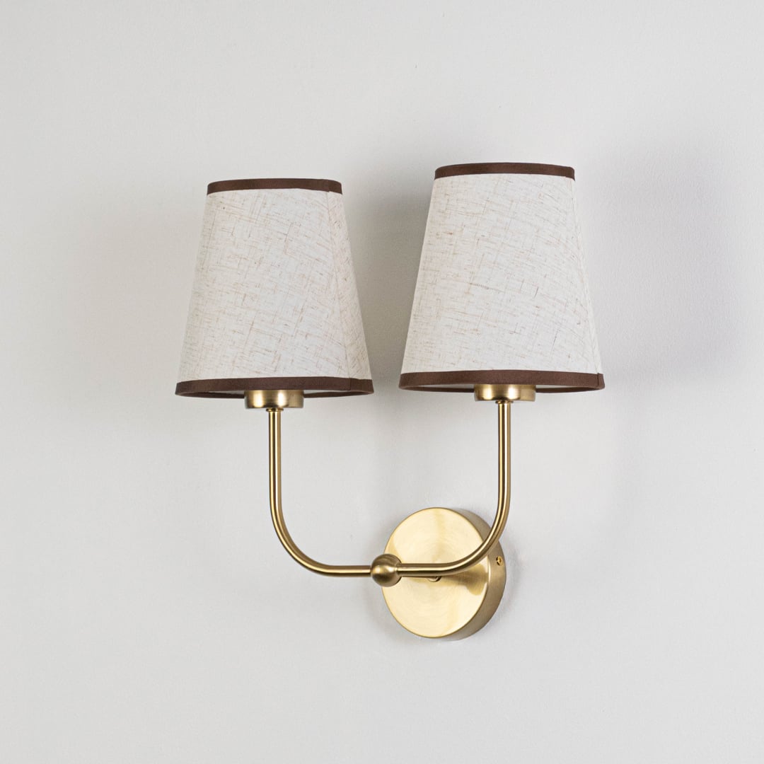 Gold metal double wall sconce with cream textured shades shown on a plain white background for product clarity.