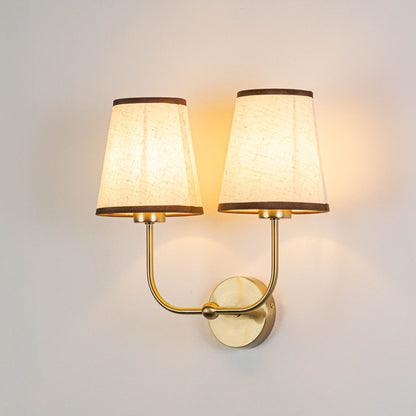 Gold metal double wall sconce with cream textured shades illuminated on a bright white background for clear visibility.