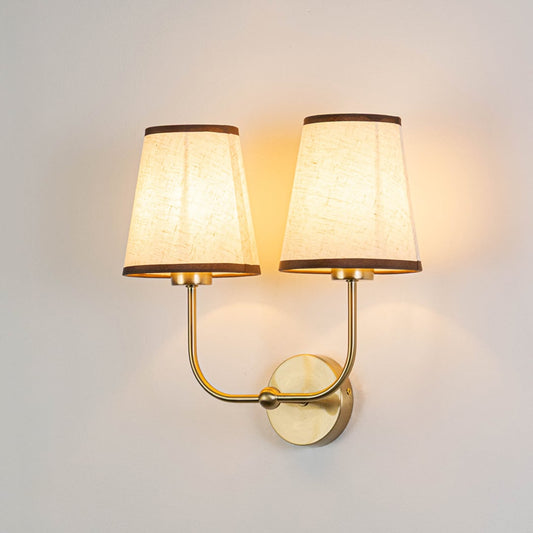 Gold metal double wall sconce with cream textured shades illuminated on a bright white background for clear visibility.