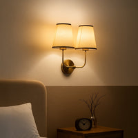 Gold metal double wall sconce with cream textured shades adding warm ambient lighting to a modern home interior.