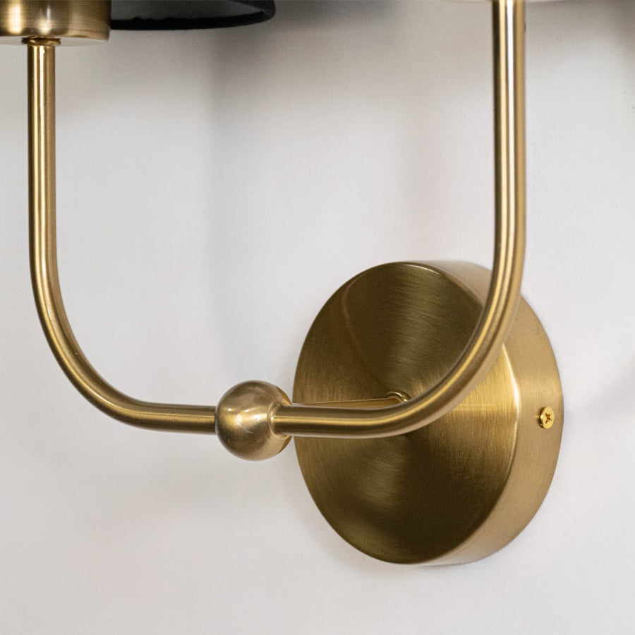 Closeup of gold metal double wall sconce with black fabric shades highlighting modern elegant detailing.