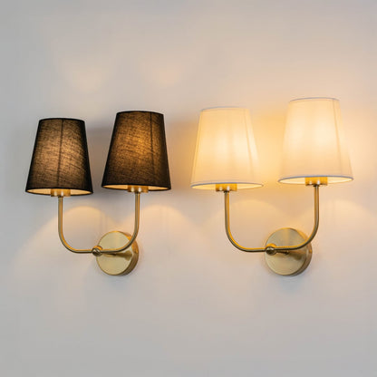 Double wall sconce with gold metal frame and black fabric shades illuminated on a clean white background.