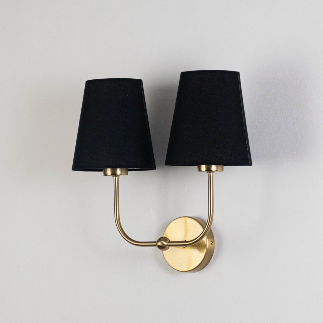Gold double wall sconce with black fabric shades shown on a white background for clear product detailing.