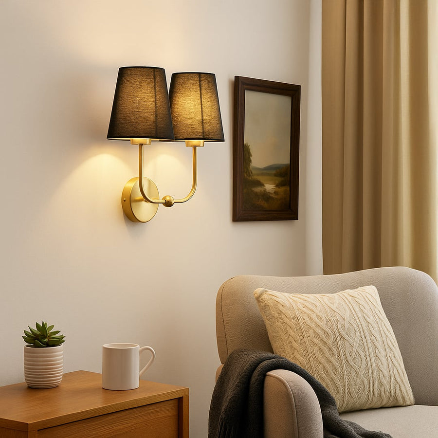 Gold metal double wall sconce with black fabric shades adding warm stylish lighting to a modern home interior.