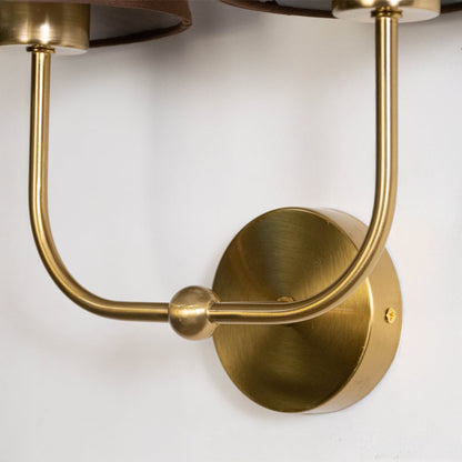 Closeup of gold metal double wall sconce with brown fabric shades highlighting elegant detailing and smooth finish.