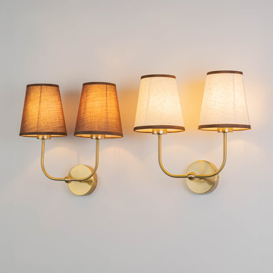 Double wall sconce with gold frame and brown fabric shades illuminated on a clean white background.