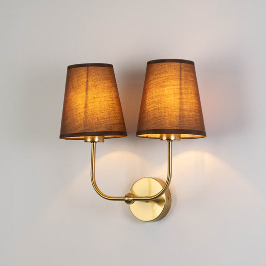 Contemporary wall light in gold metal finish with dual fabric shades for bedroom or living room ambient lighting decor white background.