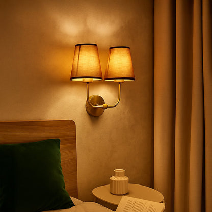 Gold metal double wall sconce with brown fabric shades adding warm ambient lighting to a modern home interior.