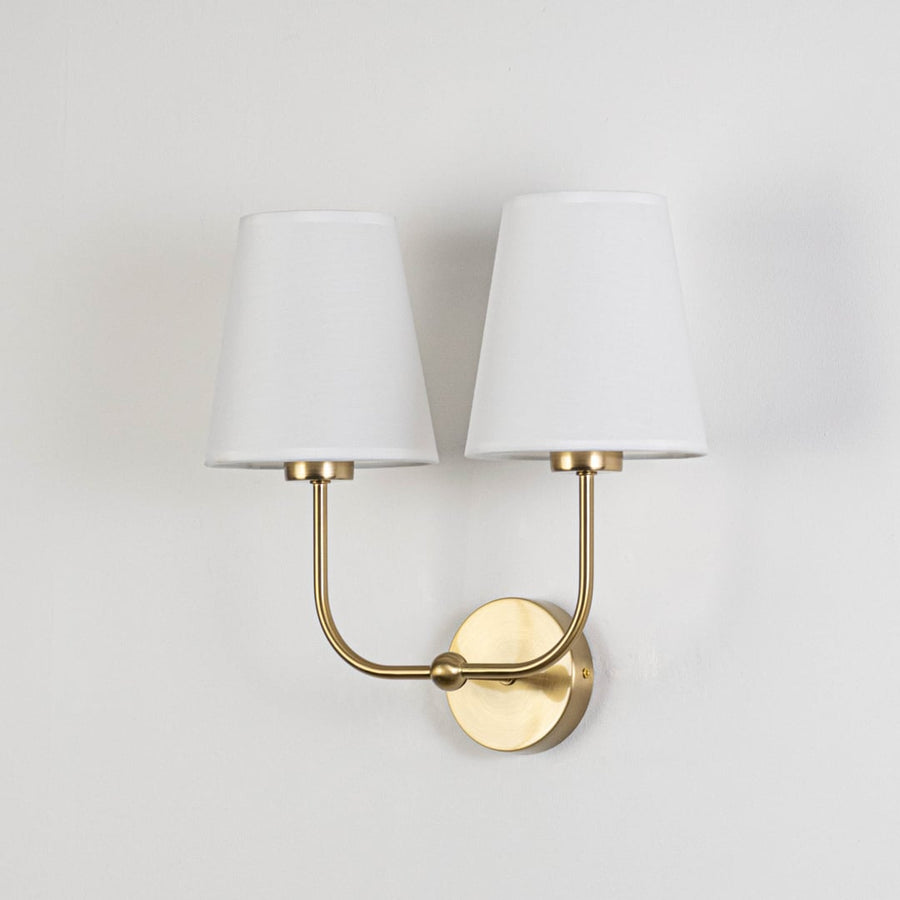 Gold metal double wall sconce with white fabric shades shown on a white background for clear product detailing.