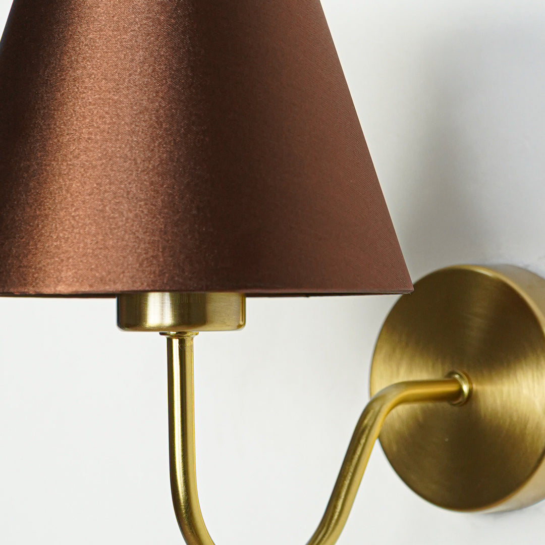 Closeup wall light in gold metal finish with brown fabric shade for bedroom or living room decor lighting white background.
