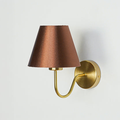 Modern wall light in gold metal finish with brown fabric shade for bedroom or living decor lighting placement white background.