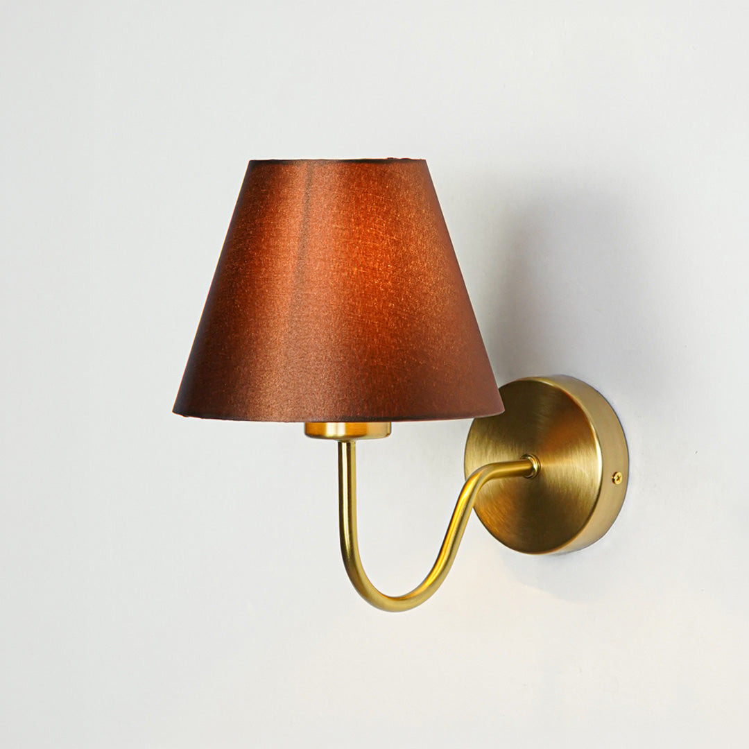 Contemporary wall light in gold metal finish with dark fabric shade for bedroom or living decor lighting white background.