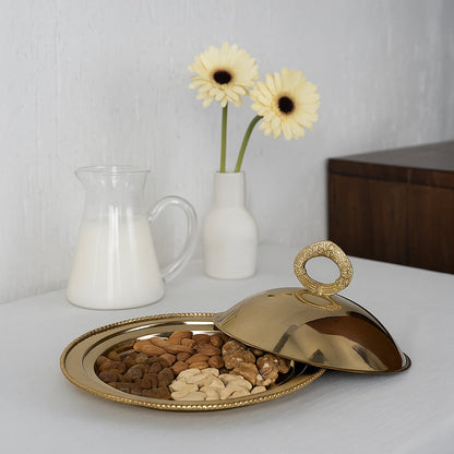 Gold brass serving tray with beaded rim filled with mixed dry fruits and lid open on a white table for a modern dining presentation.