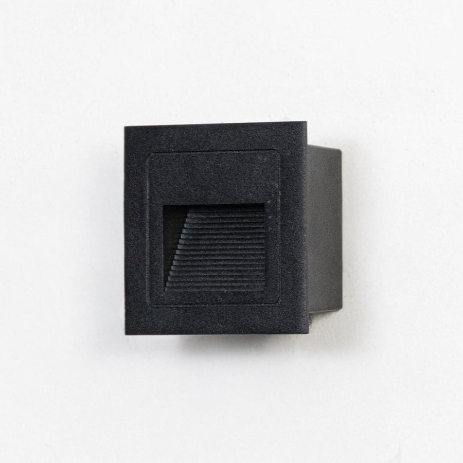 Square matte black step light with ribbed diffuser displayed off on clean white background surface.
