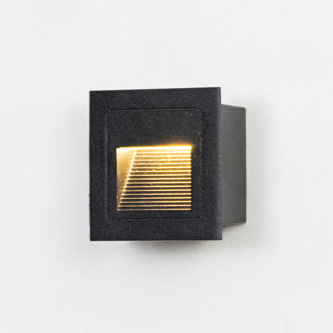 Black metal outdoor step light on white background with warm recessed glow for modern exterior decor.