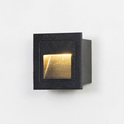 Black metal outdoor step light on white background with warm recessed glow for modern exterior decor.