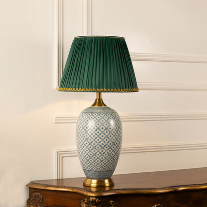 Grey patterned ceramic table lamp with green pleated shade displayed on a side table creating sophisticated ambient lighting.
